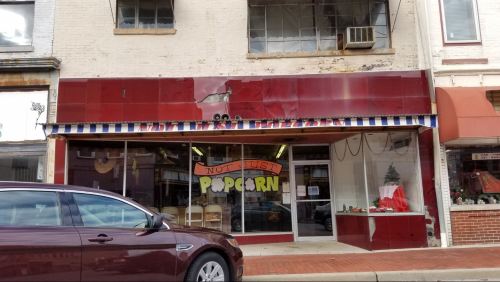 A storefront with a red facade and a striped awning, featuring a sign that reads "Not Just Popcorn."