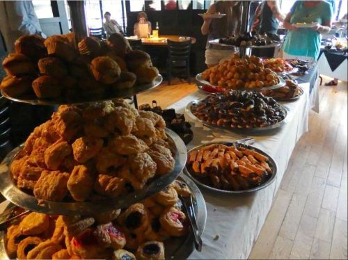 A variety of baked goods displayed on tiered trays, including pastries, cookies, and muffins in a dining setting.