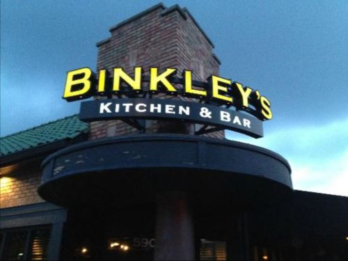 Sign for Binkley's Kitchen & Bar, illuminated against a cloudy evening sky.