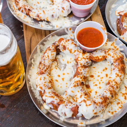 Two large pretzels topped with melted cheese, served with marinara sauce, alongside a glass of beer.