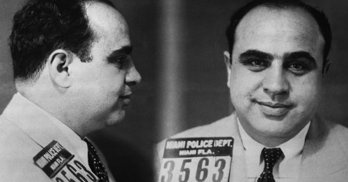 Mugshot of a man with a prominent smile, wearing a suit, identified as from the Miami Police Department.