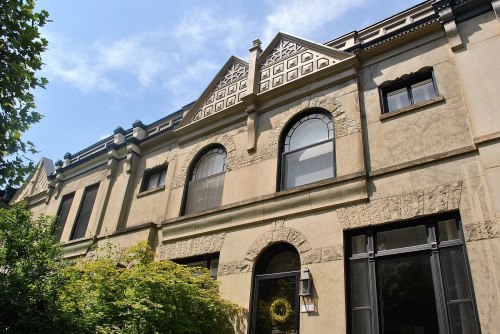 Historic building facade with ornate architectural details and large windows, surrounded by greenery under a blue sky.