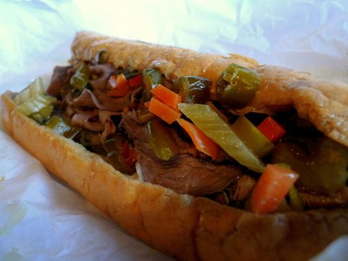 A close-up of a sandwich filled with sliced beef, green peppers, and carrots in a toasted roll.