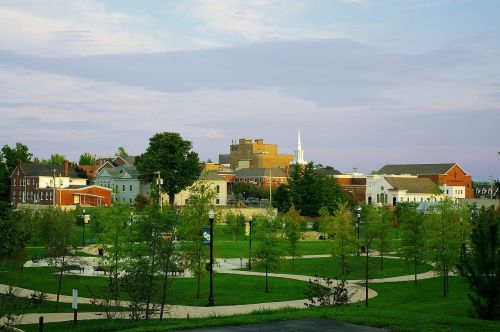 A scenic view of a small town with green parks, trees, and buildings under a pastel sky.