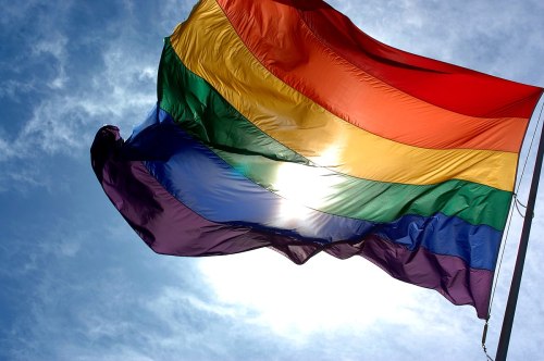 A rainbow flag waves against a bright sky, symbolizing LGBTQ+ pride and diversity.