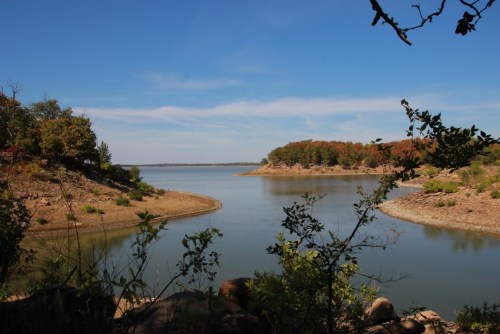A serene lake view with gentle curves, surrounded by trees and a clear blue sky.
