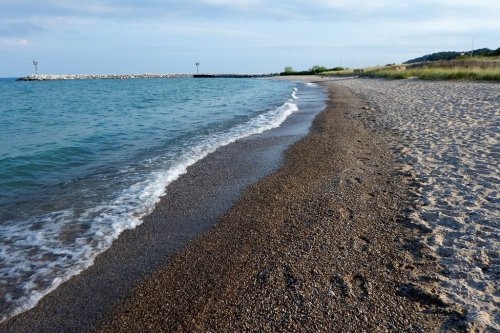 A serene beach scene with gentle waves lapping at the shore, pebbles and sand, under a cloudy sky.