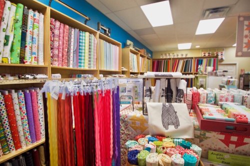 A colorful fabric store display with various rolls of fabric, spools of thread, and sewing supplies on shelves.