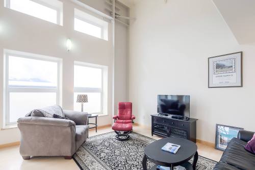 A modern living room with large windows, a red chair, a TV, and a decorative rug. Bright and airy atmosphere.
