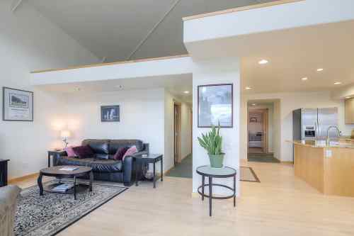 A spacious living area with a black leather sofa, coffee table, and kitchen in the background, featuring modern decor.