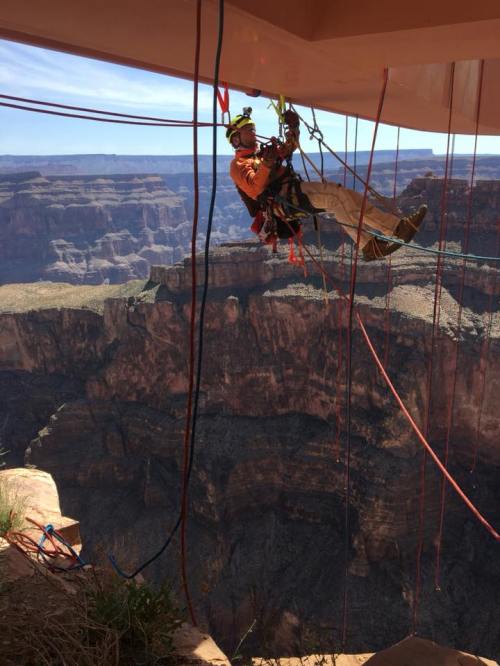 A person in safety gear rappels down a cliff, surrounded by rocky terrain and a vast canyon landscape.