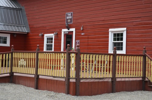 A red barn with a yellow railing and windows, featuring a sign that reads "The Barn" above the entrance.