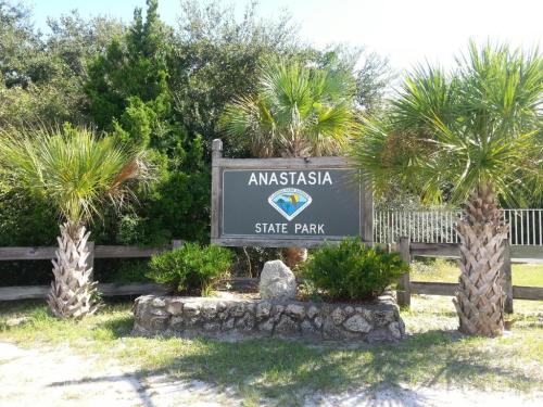 Sign for Anastasia State Park, framed by palm trees and greenery, with a clear blue sky in the background.