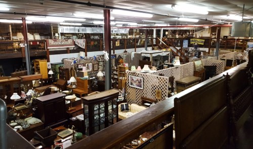 A spacious antique store filled with various furniture, lamps, and decor items, organized in distinct sections.