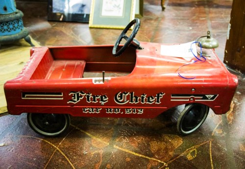 A vintage red toy fire truck with "Fire Chief" written on the side, displayed in an antique shop.