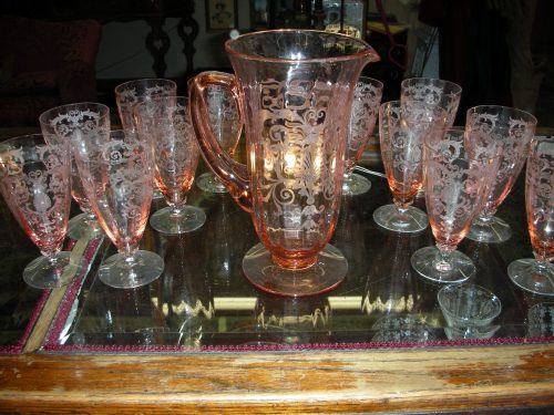 A vintage glass pitcher with matching etched glasses arranged on a glass table.