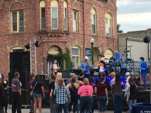 A band performs on stage in front of a crowd near a historic building during an outdoor event.