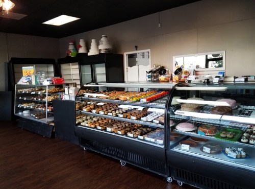A bakery display case filled with various colorful pastries, cakes, and cupcakes in a well-lit shop.