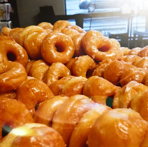 A close-up of a pile of glazed donuts, glistening under bright light.