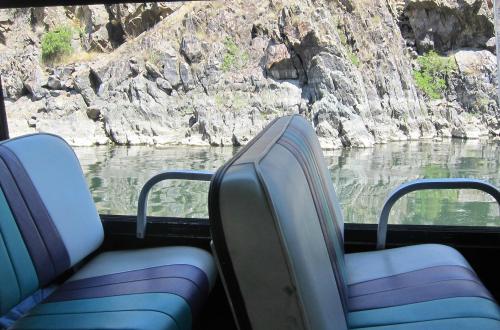 Two striped seats inside a boat, with rocky cliffs and calm water visible outside the window.