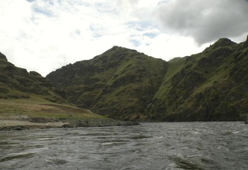 A serene river flows between lush green mountains under a cloudy sky.