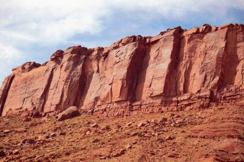 A rugged red rock formation rises against a blue sky, showcasing layers and textures in a desert landscape.