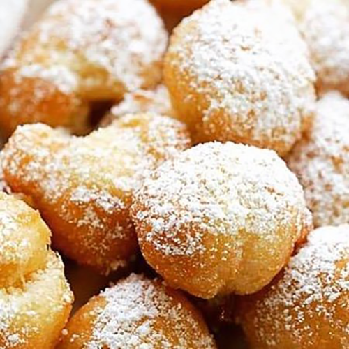 A close-up of golden, fluffy pastries dusted with powdered sugar, piled together.