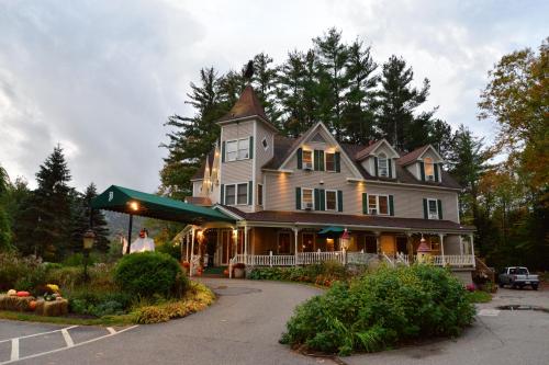 A charming multi-story house with a wraparound porch, surrounded by trees and colorful landscaping.