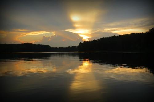Sunset over a calm lake, with reflections of clouds and trees on the water's surface.
