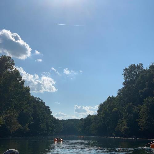 A serene river scene with clear blue skies, fluffy clouds, and lush green trees lining the banks.