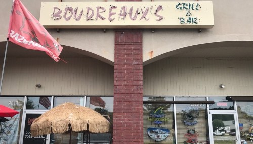 Exterior of Boudreaux's Grill & Bar, featuring a thatched umbrella and a red flag outside the entrance.