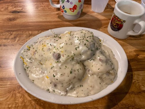 A plate of fluffy biscuits smothered in creamy sausage gravy, garnished with parsley, on a wooden table.