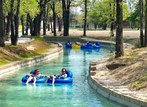 People relaxing on blue inner tubes in a winding, clear waterway surrounded by trees.