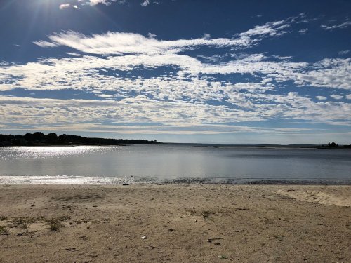 A serene beach scene with calm water, sandy shore, and a sky filled with fluffy clouds and blue hues.