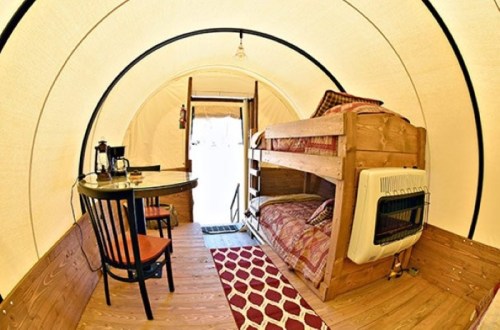 Cozy interior of a glamping tent featuring a bunk bed, dining table, and a small heater. Warm, inviting atmosphere.