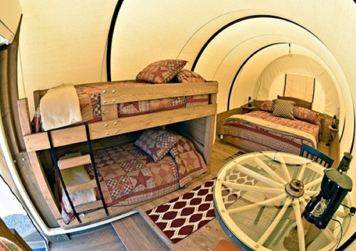 Cozy interior of a glamping tent featuring bunk beds and a double bed, with rustic decor and a round table.