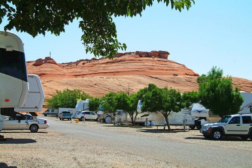 A scenic RV park with several parked trailers and a backdrop of red rock formations under a clear blue sky.