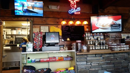 A cozy restaurant interior with a bar, TVs showing sports, and a menu board. Snacks and drinks are displayed on the counter.