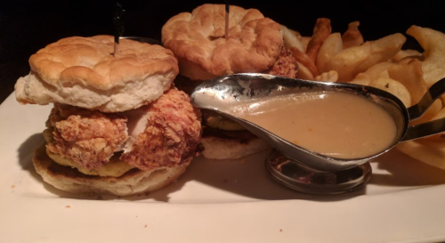 Two fried chicken biscuits with gravy on the side, accompanied by crispy fries.