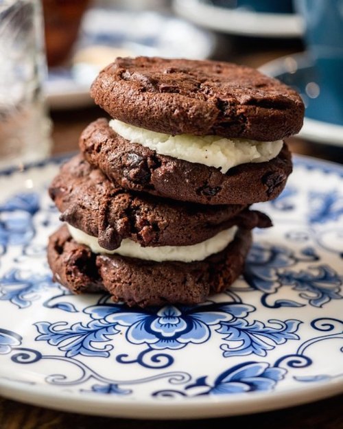 A stack of three chocolate cookies with white cream filling, served on a decorative blue and white plate.