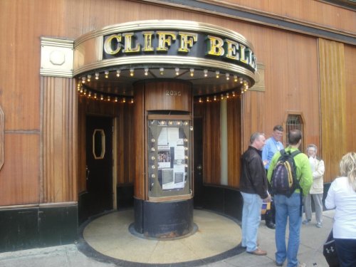 Entrance of Cliff Bell's, a vintage-style venue with wooden paneling and marquee lights, with people gathered outside.