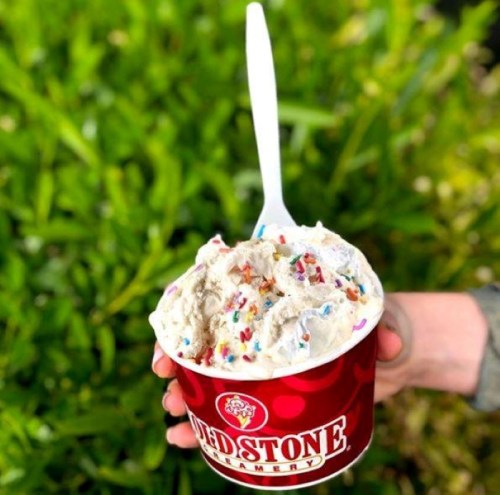 A hand holding a cup of ice cream topped with colorful sprinkles, set against a green background.