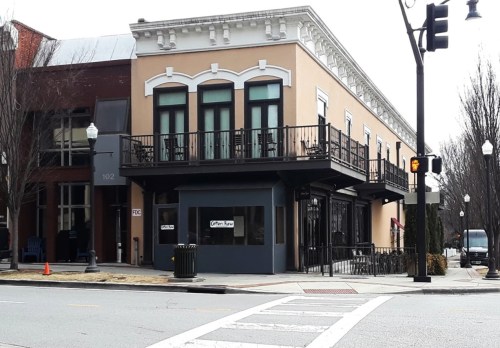A corner building with a balcony, featuring large windows and a sign, located on a city street.