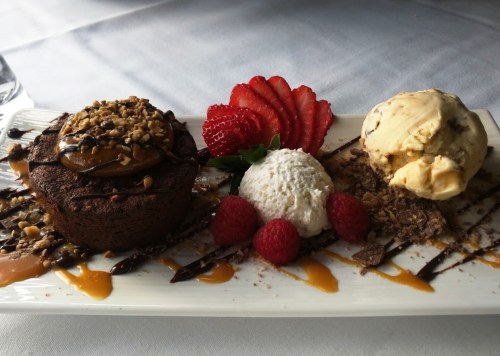A dessert plate featuring a chocolate cake, ice cream, whipped cream, strawberries, raspberries, and drizzled sauce.