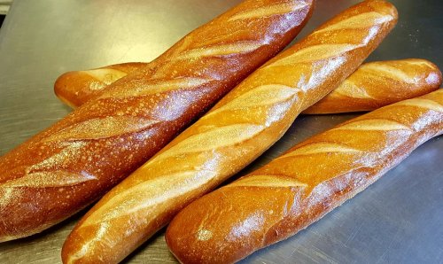 Four freshly baked baguettes with a golden crust, arranged on a metallic surface.
