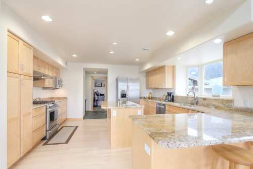 Modern kitchen with light wood cabinets, granite countertops, stainless steel appliances, and ample natural light.