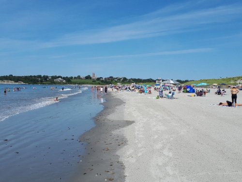 A sunny beach scene with people swimming, sunbathing, and enjoying the shoreline on a clear day.