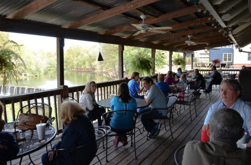 A group of people sitting at tables on a covered porch overlooking a river and waterfall.