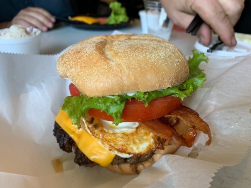 A delicious burger with lettuce, tomato, cheese, bacon, and a fried egg on a toasted bun, served on a paper wrapper.