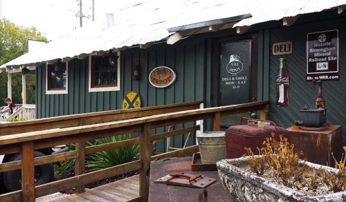 A rustic deli and grill with a wooden ramp, vintage signs, and railroad decor, set in a historic location.